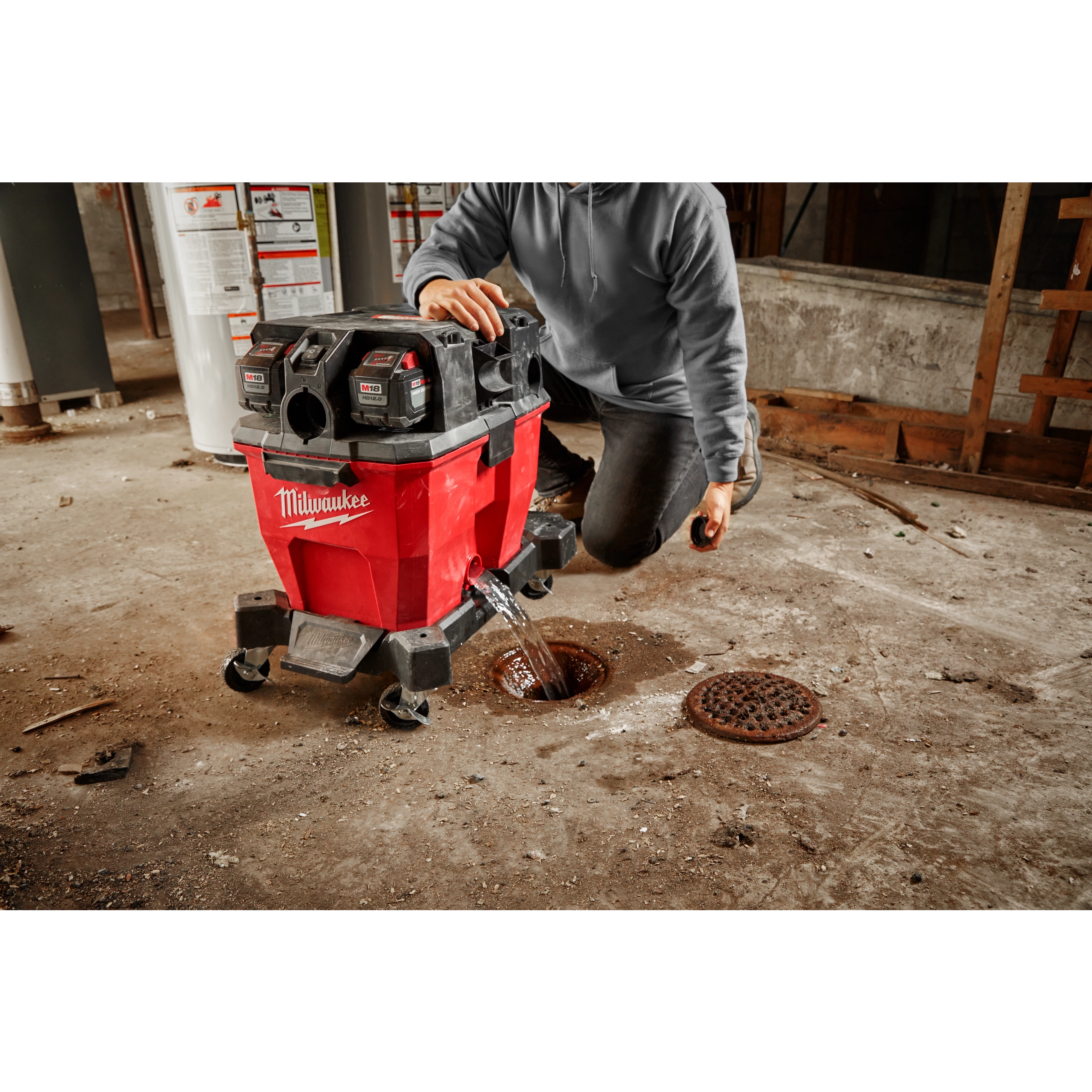 Person using a red 9 Gallon Wet/Dry Vacuum Tank to clean a concrete floor, draining water into a floor drain.