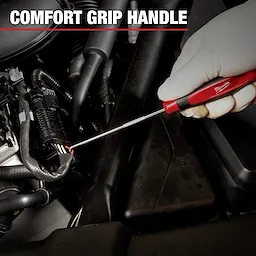 A gloved hand uses a Milwaukee Mechanic Hand Tool with a comfort grip handle to work on a car engine. The tool is a long, thin screwdriver or pick inserted into an automotive component.