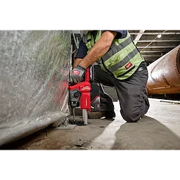 A worker in safety gear uses an M18 FUEL™ 5/8" SDS Plus Rotary Hammer with Dust Extractor Kit to drill into a metal surface inside an industrial setting.