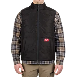 A person is wearing a black FREEFLEX™ Lightweight Insulated Vest over a plaid shirt. The vest has a front zipper and a red Milwaukee logo patch on the lower left side. The person’s hands are resting by their sides.