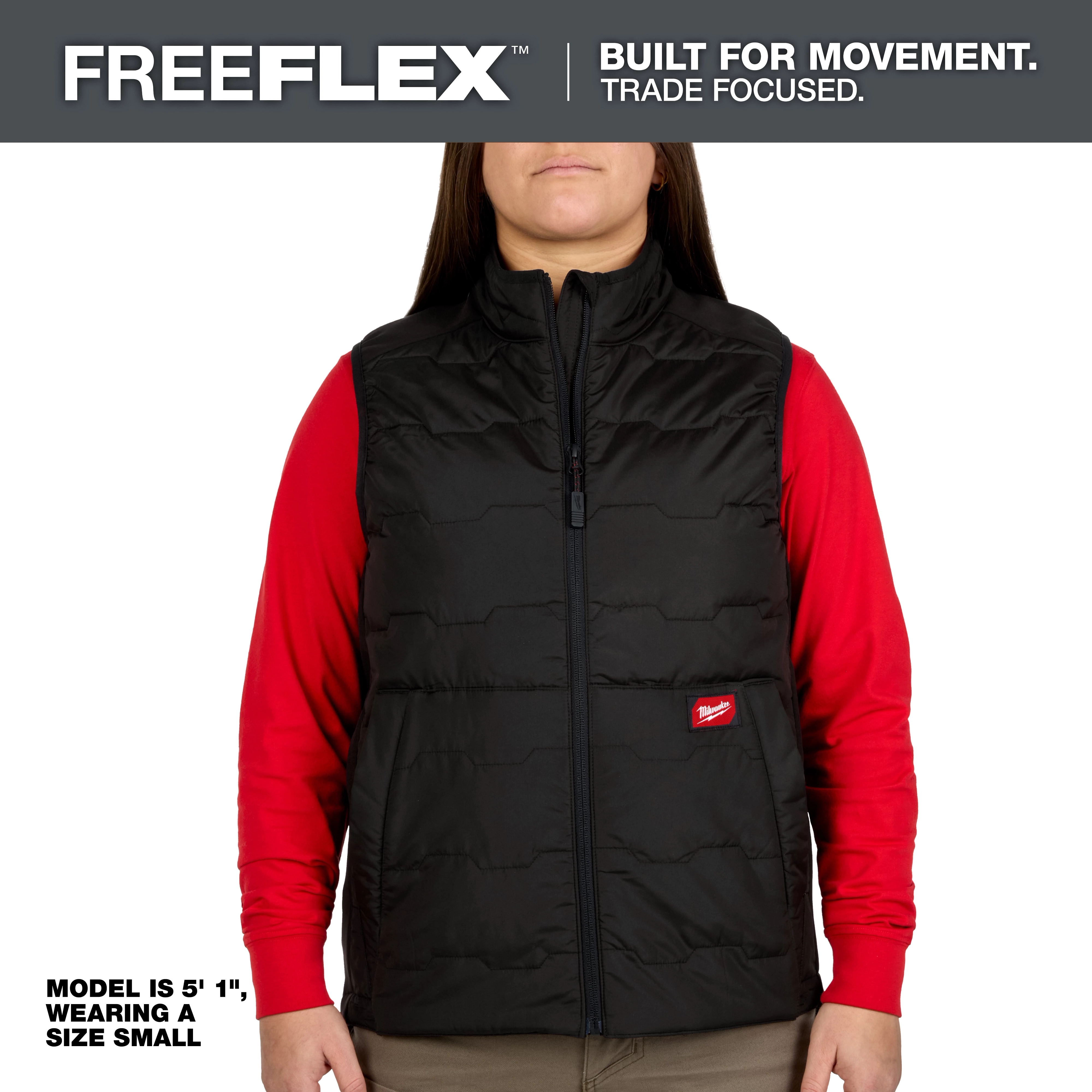 A model wearing a black Milwaukee Freeflex vest paired with a red long-sleeve shirt. The vest has a front zipper and a small red logo patch. The model's height is 5'1" and is wearing a size small.