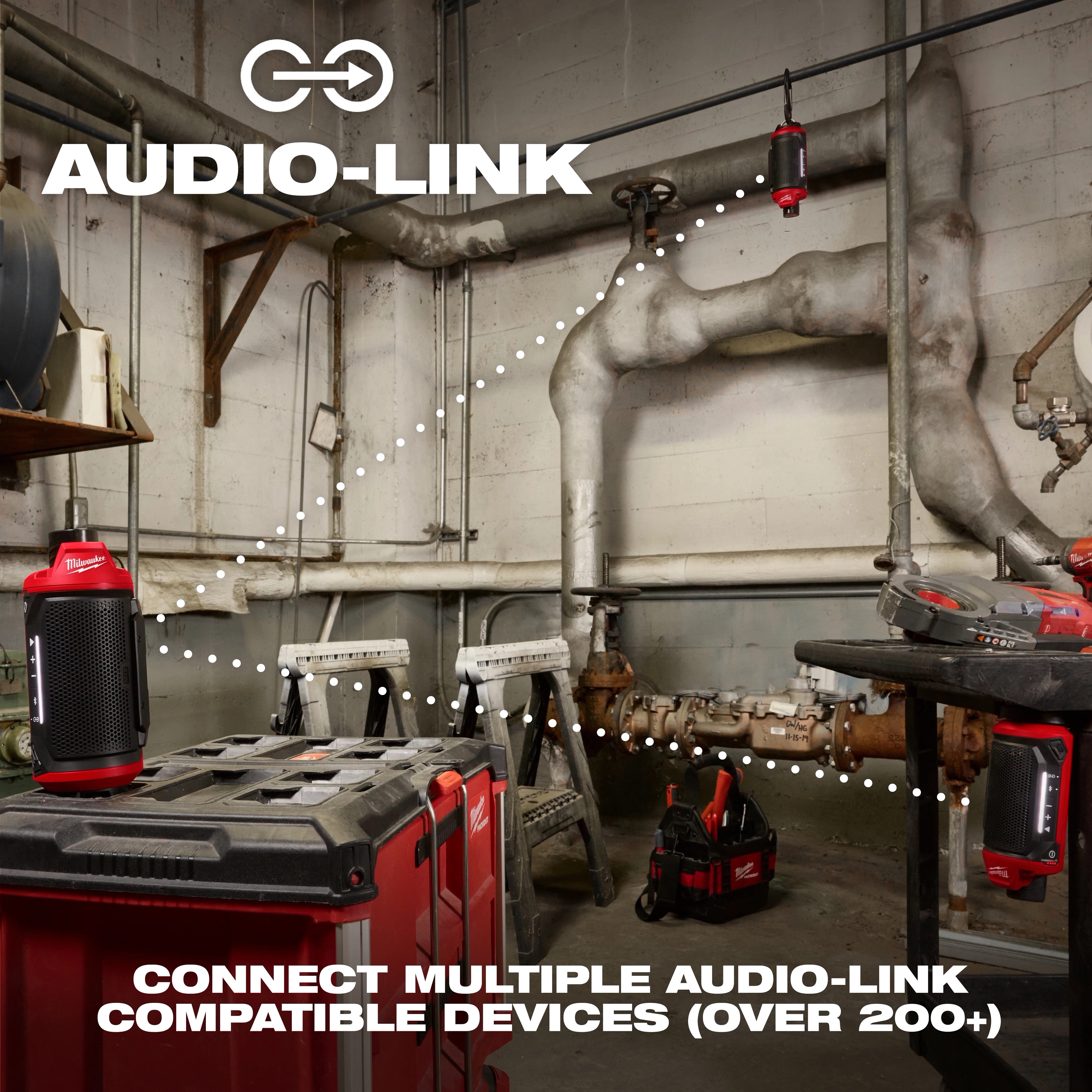 A workshop with an M12™ Bluetooth® Jobsite Speaker w/ PACKOUT™ Compatibility is displayed. The image highlights the connectivity feature "Audio-Link" with multiple speakers linked through dotted lines. The text reads, "CONNECT MULTIPLE AUDIO-LINK COMPATIBLE DEVICES (OVER 200+)." Various tools are also visible in the background.