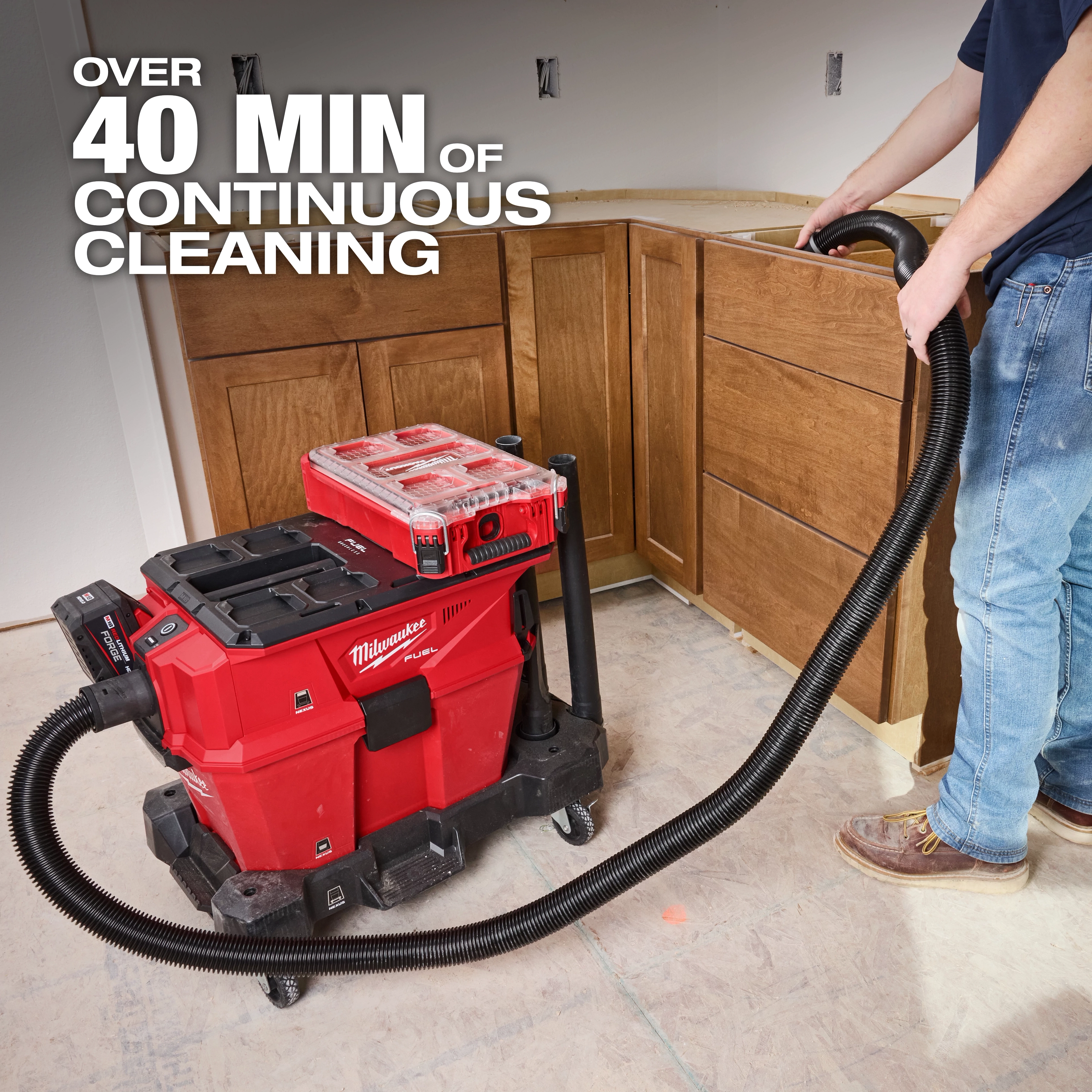 The Milwaukee M18 FUEL™ NEXUS™ 6 Gallon Wet/Dry Vacuum with PACKOUT™ Compatibility is used on a job site. It provides over 40 minutes of continuous cleaning. A worker uses the vacuum in a construction area with wooden cabinets.