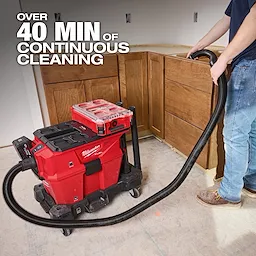 The Milwaukee M18 FUEL™ NEXUS™ 6 Gallon Wet/Dry Vacuum with PACKOUT™ Compatibility is used on a job site. It provides over 40 minutes of continuous cleaning. A worker uses the vacuum in a construction area with wooden cabinets.