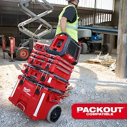 Person hauling stacked Milwaukee Packout storage boxes on a construction site. The M18 BLUETOOTH JOBSITE RADIO + CHARGER is seen on top of the stack.