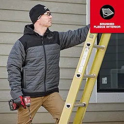 A person wearing a WORKSKIN™ Low-Profile Beanie, gray and black zip-up jacket, and brown pants is holding a red power tool and climbing a yellow ladder. A red label in the top right corner reads "BRUSHED FLEECE INTERIOR."