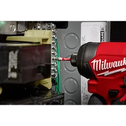 A Milwaukee power tool is being used with a SHOCKWAVE™ 2” Impact Square Recess #2 Power Bit to tighten screws on an electrical panel. The bit is attached to the power tool and is making contact with the screw head. Various wiring components are visible in the background.