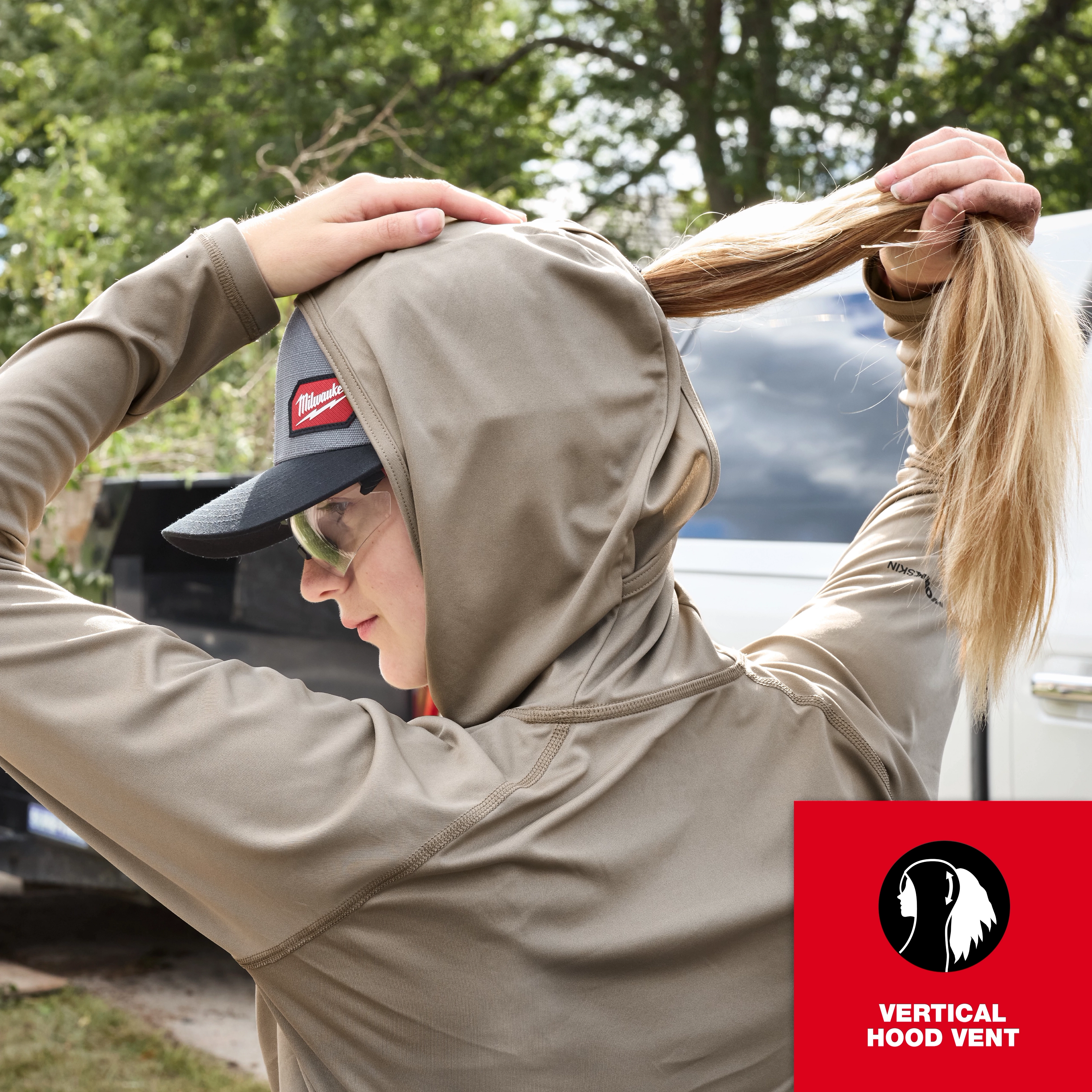 A person adjusts their hood while wearing a long-sleeve Women's WORKSKIN Hooded Sun Shirt.