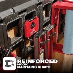 Milwaukee PACKOUT 4" Straight Hook attached to a storage system, holding measuring tools with a nearby paper towel holder. Text reads "Reinforced Hook Maintains Shape."