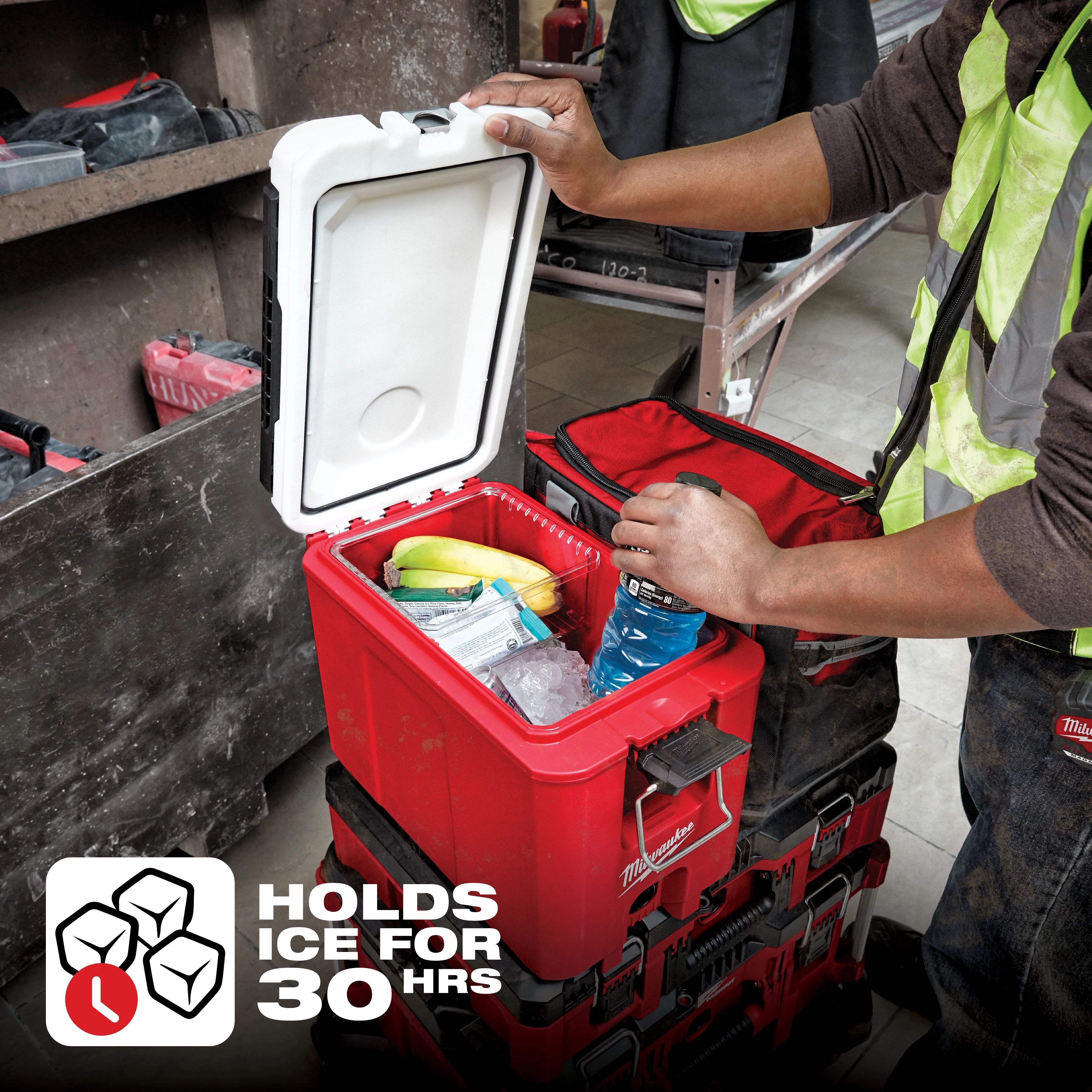 The 48-22-8460%20App%20Shot is a red, insulated cooler box with an open lid, revealing ice, drinks, and snacks inside. A person wearing a reflective vest is accessing the cooler. A label indicates it can hold ice for 30 hours.