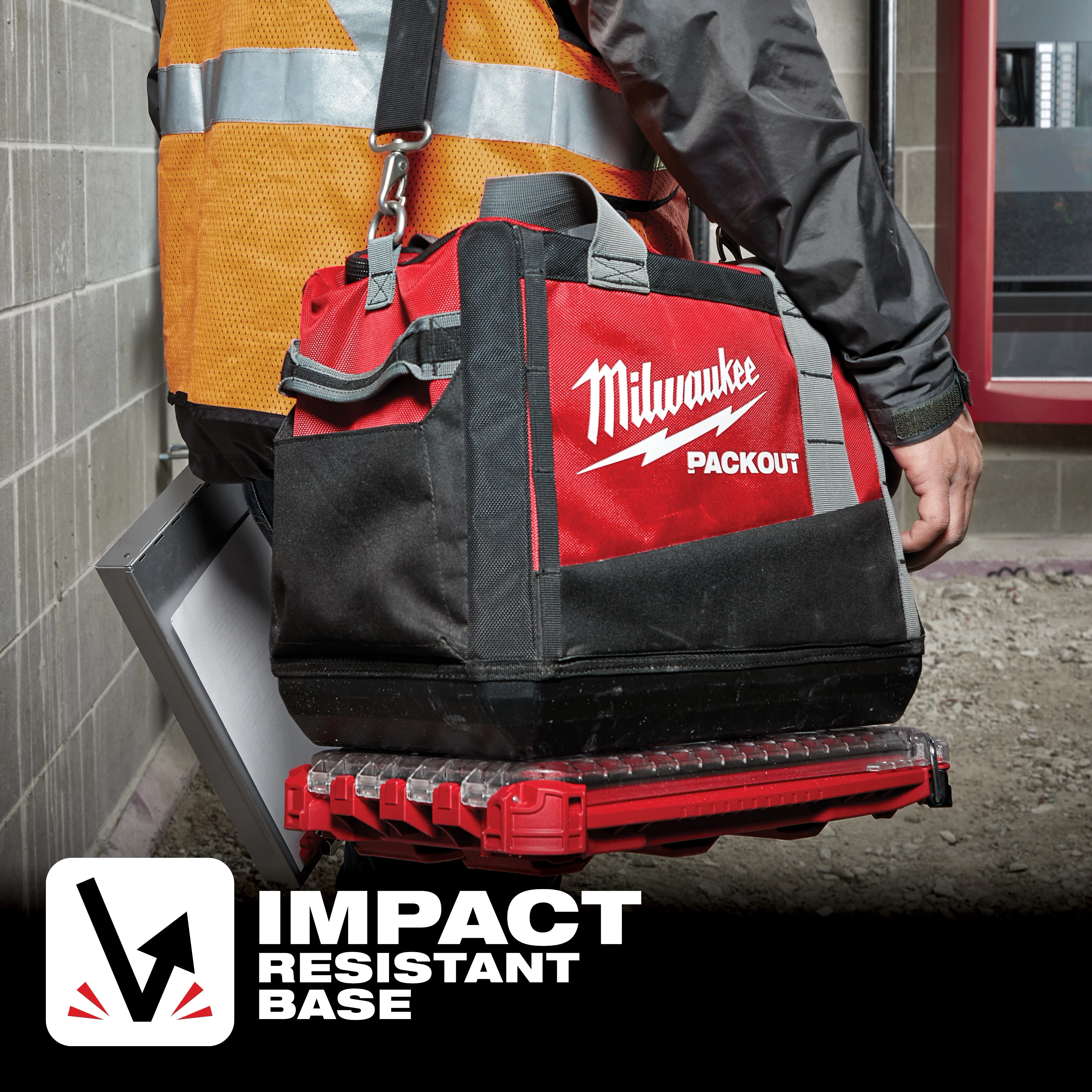 A person carries a Milwaukee Packout tool bag with App%20Shot%20Overlay, featuring an impact-resistant base, in a construction area.