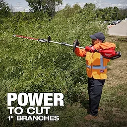 A person in an orange safety vest uses a Milwaukee power tool to trim large bushes. The text on the image reads "Power to cut 1" branches." Trees and a parking lot are in the background.