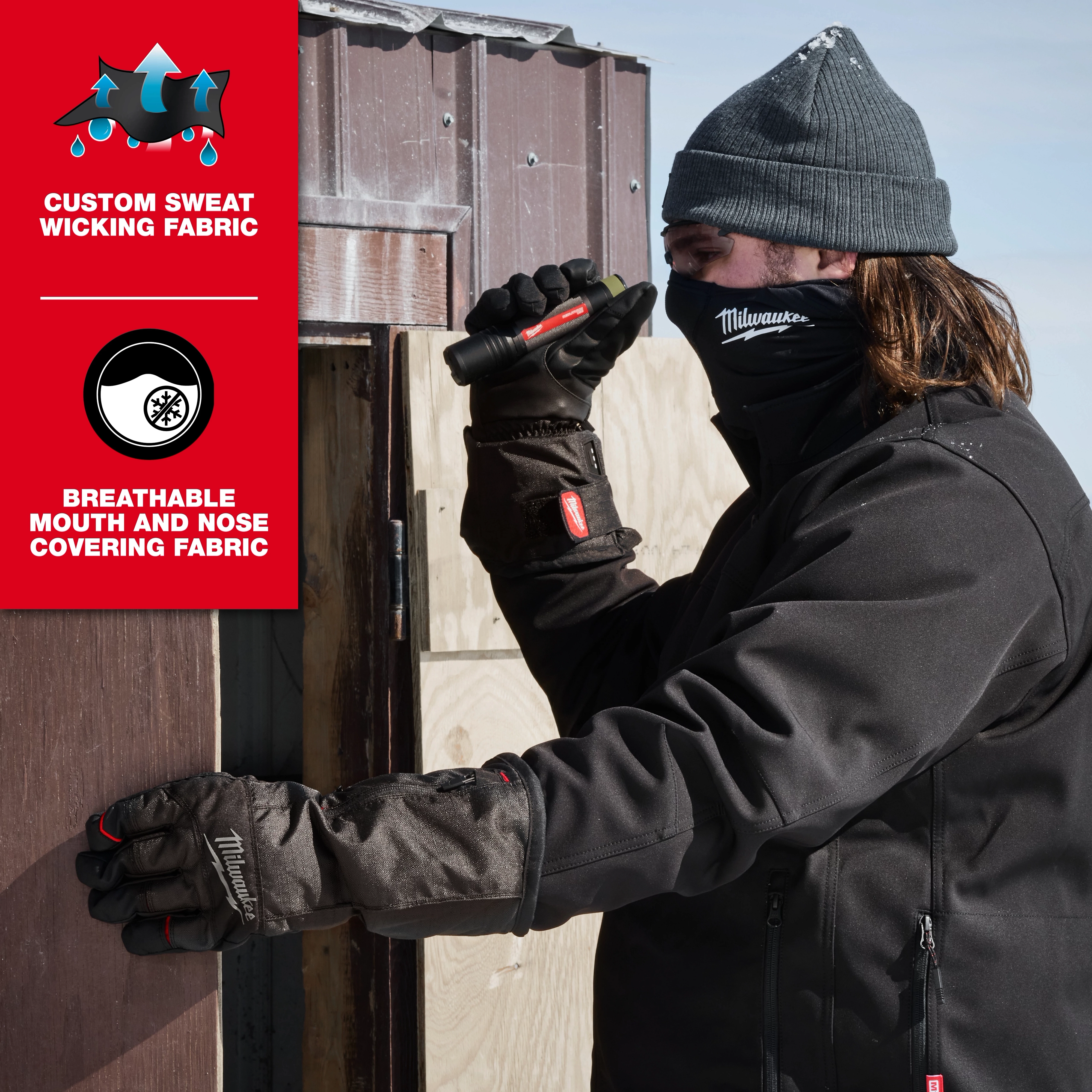 Person in cold weather gear works with a flashlight by a wooden structure. Wearing WORKSKIN™ Balaclava beneath a beanie. The product is highlighted for its custom sweat-wicking and breathable mouth and nose covering fabric.