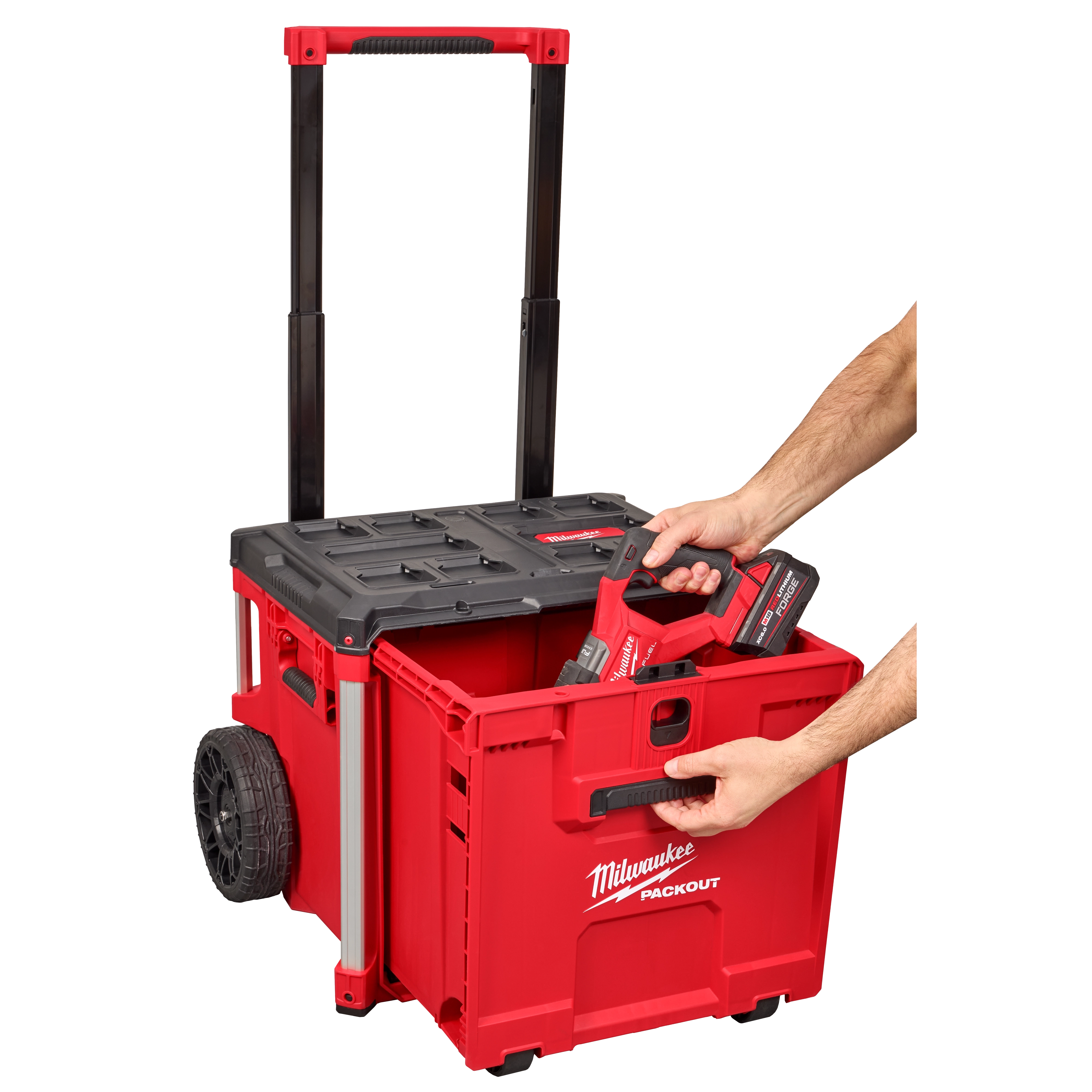 A person places a tool into a red PACKOUT™ Rolling Drawer Tool Box by Milwaukee, which has an extended handle and large wheels for easy transport.
