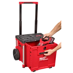 A person places a tool into a red PACKOUT™ Rolling Drawer Tool Box by Milwaukee, which has an extended handle and large wheels for easy transport.