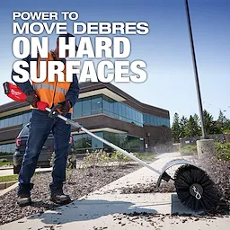 A worker wearing a safety vest uses a Milwaukee electric power tool with a rotating brush attachment to clear debris from a pathway outside a modern office building. Text on the image reads, "Power to move debris on hard surfaces."