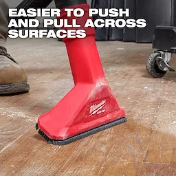 The image shows a red Milwaukee AIR-TIP™ 2-1/2" Rocking Utility Nozzle with Brushes being used on a wooden floor. The nozzle is attached to a vacuum and has brushes at its base. Text on the image reads, "Easier to push and pull across surfaces."