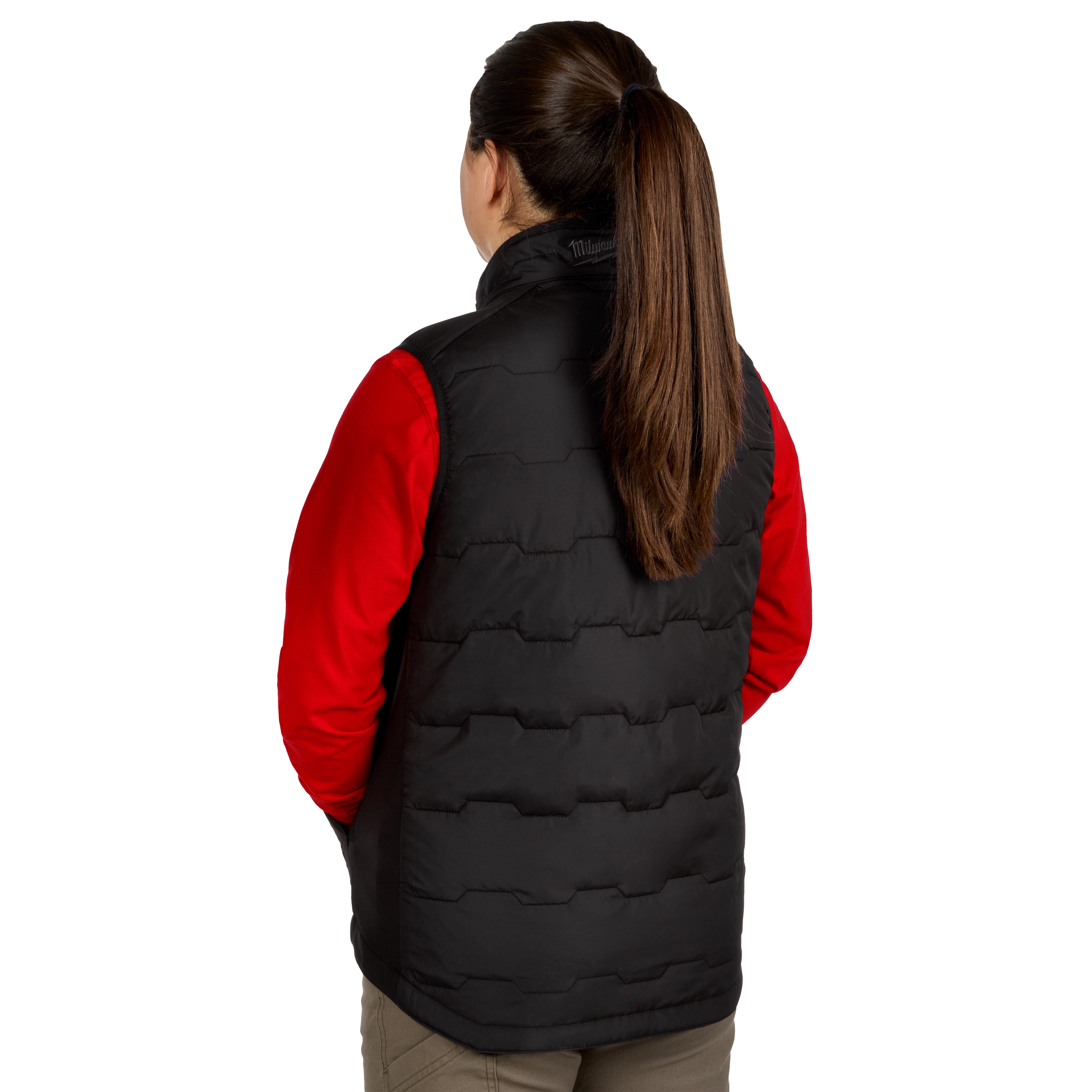 A woman with long brown hair in a ponytail is shown from the back wearing a black Women's FREEFLEX™ Lightweight Insulated Vest over a red long-sleeve shirt. The vest features a quilted pattern and a high collar.