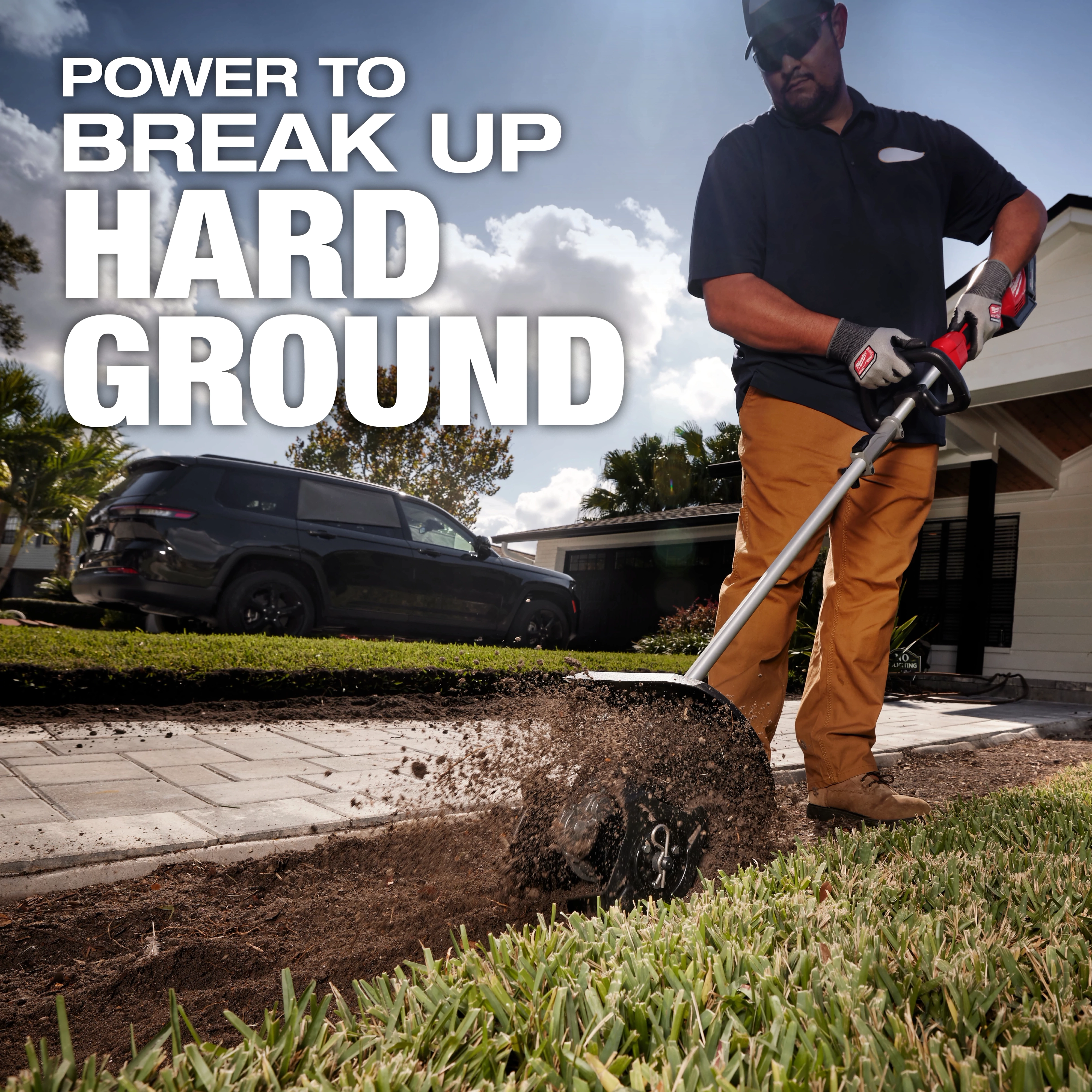 A person uses a power tool to break up hard ground in a yard. The background shows a house, a black SUV, and a partly cloudy sky. The text on the image reads, "POWER TO BREAK UP HARD GROUND."