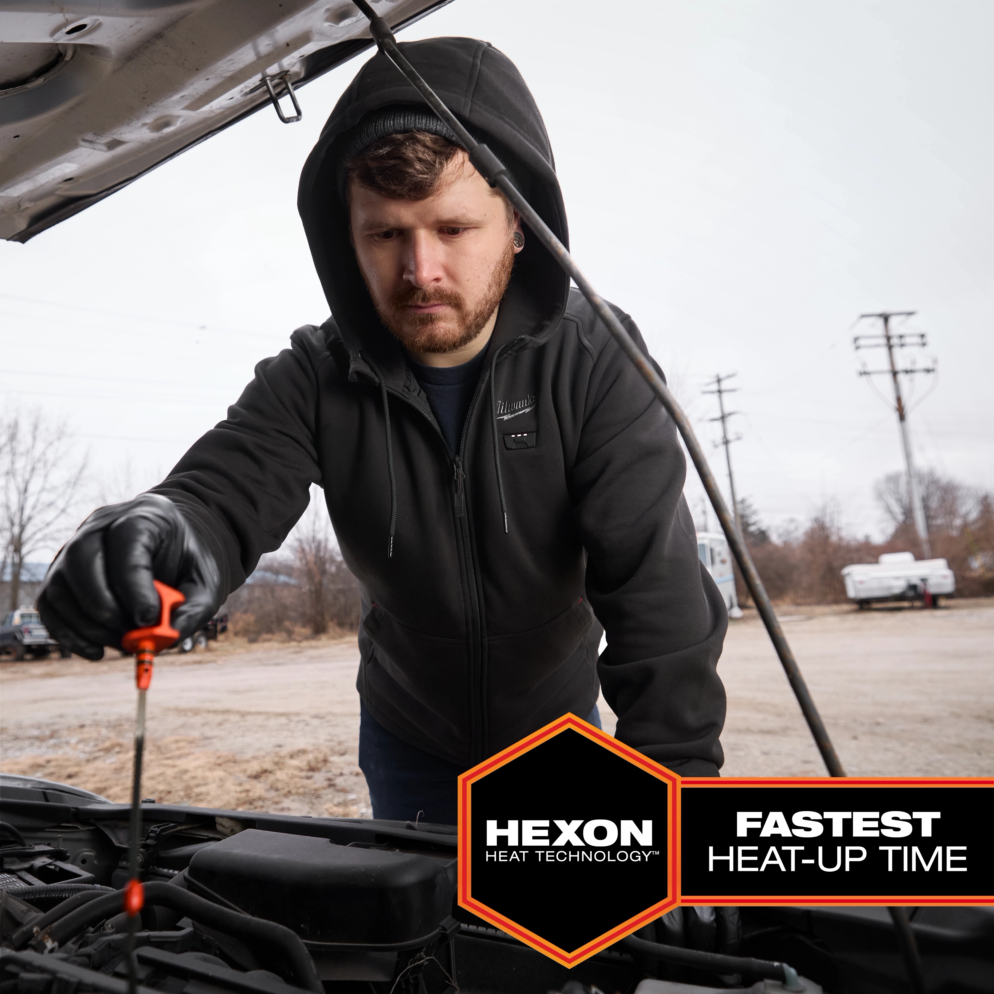 Person wearing the M12™ Heated Hoodie works under the hood of a car. The hoodie uses Hexon Heat Technology, which has the fastest heat-up time.