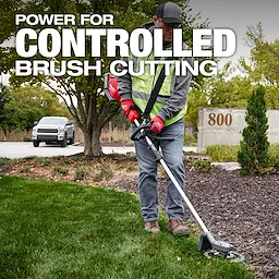 A person in a safety vest uses a brush cutter on a grassy and mulched area near a concrete sign marked "800." A white vehicle is parked in the background. The text overlay reads, "Power for Controlled Brush Cutting."