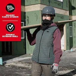 The WORKSKIN™ Balaclava is worn by a person at a construction site. They are also wearing a grey helmet, a green and black vest over a maroon top, beige pants, and gloves. The image highlights the balaclava's brushed fleece interior and durable exterior shell features.