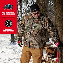 A person wearing camo jacket, tan pants, and red gloves stands beside a tree in snowy woods. The black WORKSKIN™ Low-Profile Beanie is on their head. Text on the image highlights "Custom Sweat Wicking Fabric" and "Trade Built 360° Stretch."