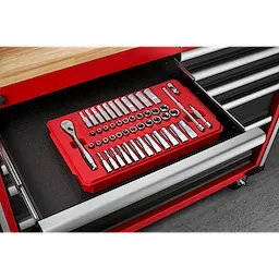 A red tray organizer containing various socket wrenches and accessories is arranged neatly inside an open drawer of a red and black tool chest. The tool chest has multiple drawers and a wooden top surface above the open drawer. The floor beneath is concrete.