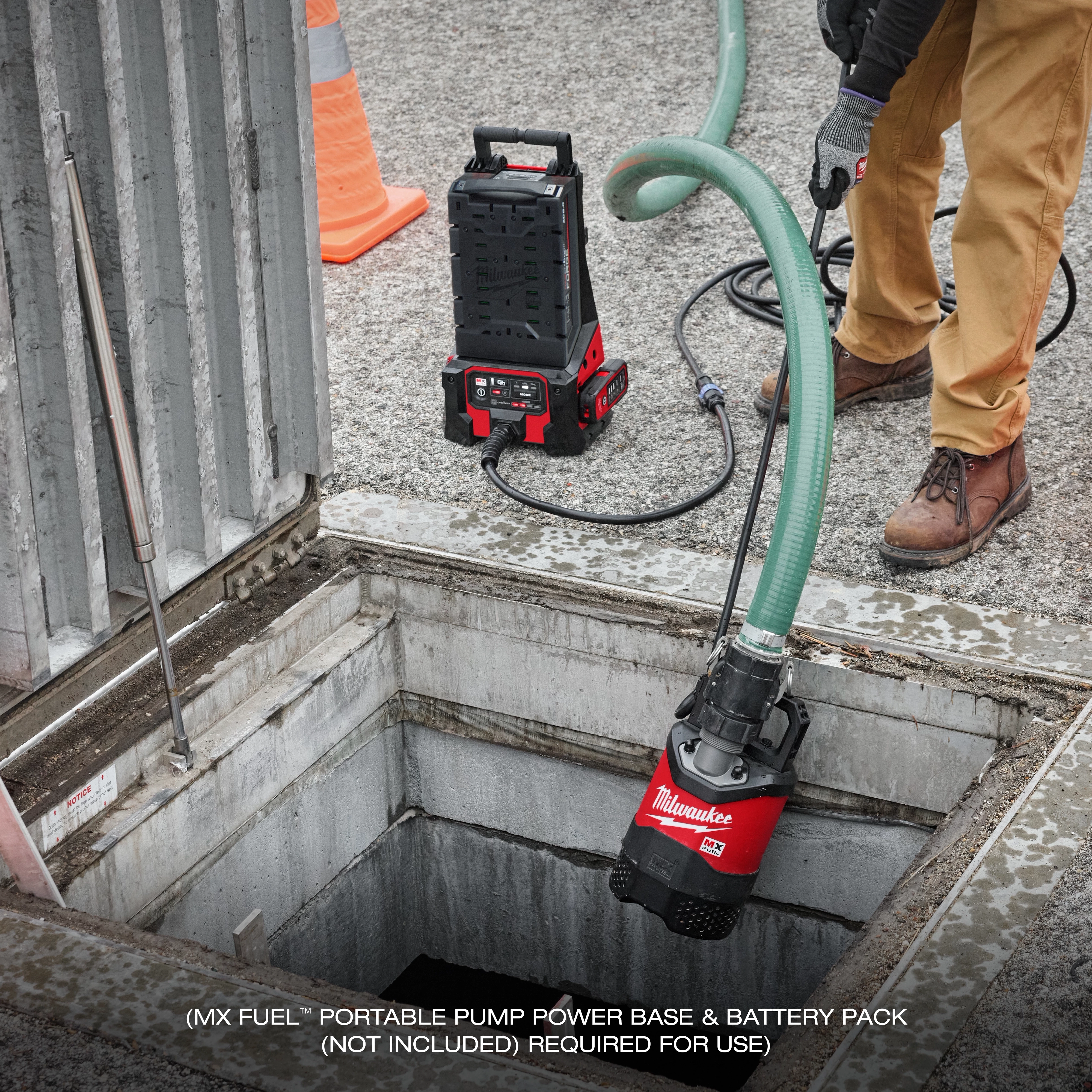 A worker operates the MX FUEL™ 1HP 2" Submersible Pump, lowering it into a water-filled pit at a construction site. The equipment is connected to a portable pump power base. Text at the bottom reads "MX FUEL™ portable pump power base & battery pack (not included) required for use."