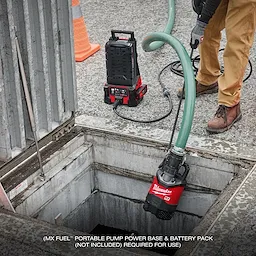 A worker operates the MX FUEL™ 1HP 2" Submersible Pump, lowering it into a water-filled pit at a construction site. The equipment is connected to a portable pump power base. Text at the bottom reads "MX FUEL™ portable pump power base & battery pack (not included) required for use."