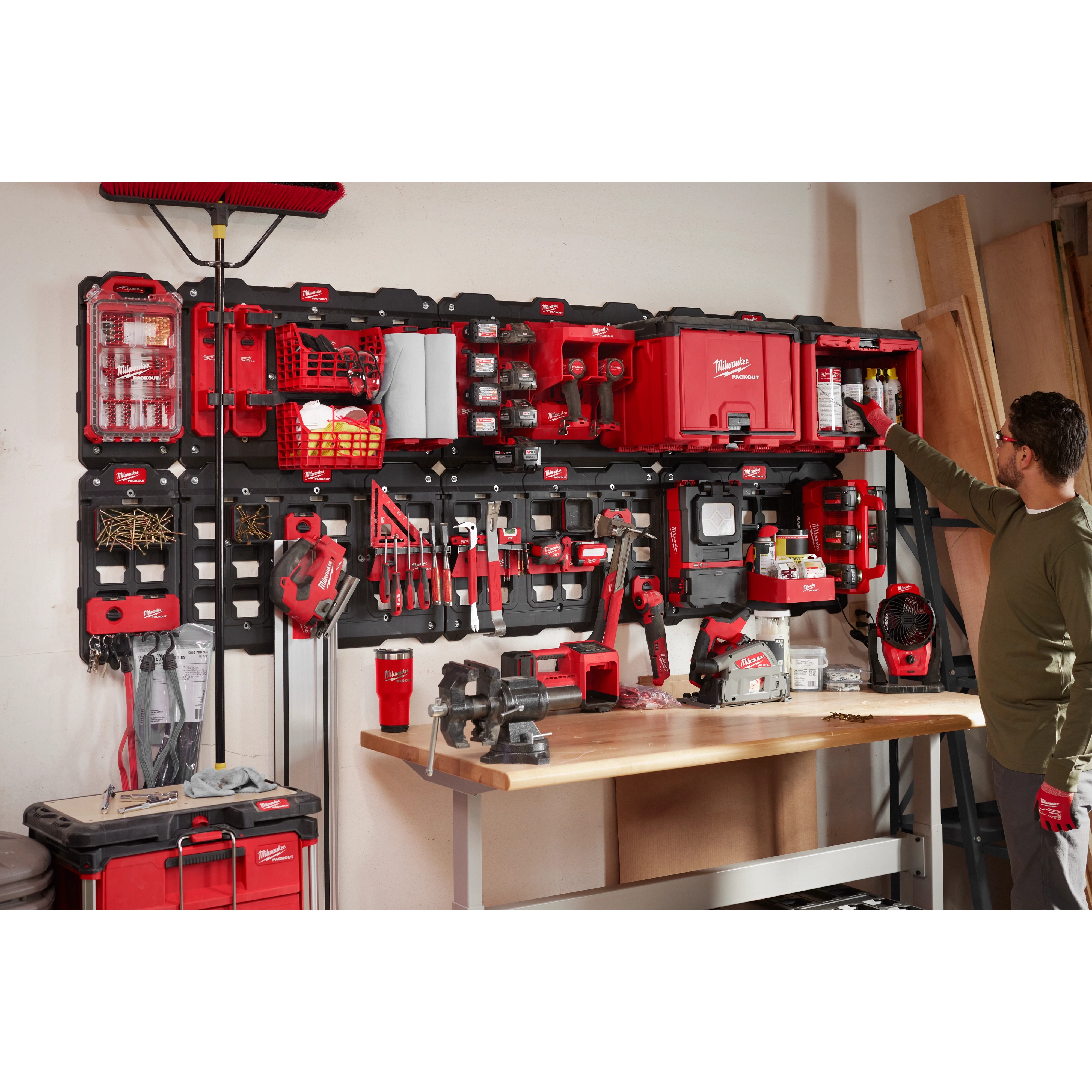Man organizing tools on a March 2023 Packout Shop Storage unit with red and black tool boxes and various tools mounted on a wall.