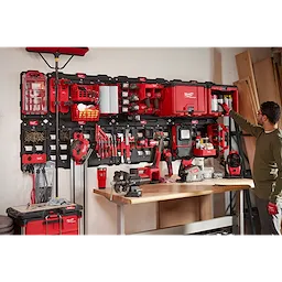 Man organizing tools on a March 2023 Packout Shop Storage unit with red and black tool boxes and various tools mounted on a wall.