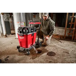 12 Gallon Wet/Dry Vacuum Tank is draining water into a floor drain in an industrial setting. A person is kneeling nearby.