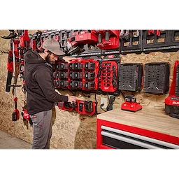 A person stands near a wall-mounted charging station, organizing tools and batteries labeled Power Manager – 20 Amp Circuit. The setup includes various power tools, chargers, and a red tool chest with drawers.