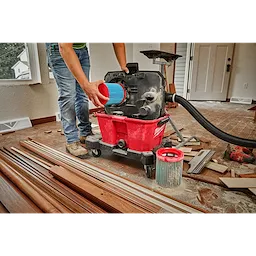Person installing a blue MILWAUKEE Large Wet/Dry Vacuum High Efficiency Filter into a red vacuum unit on a construction site.