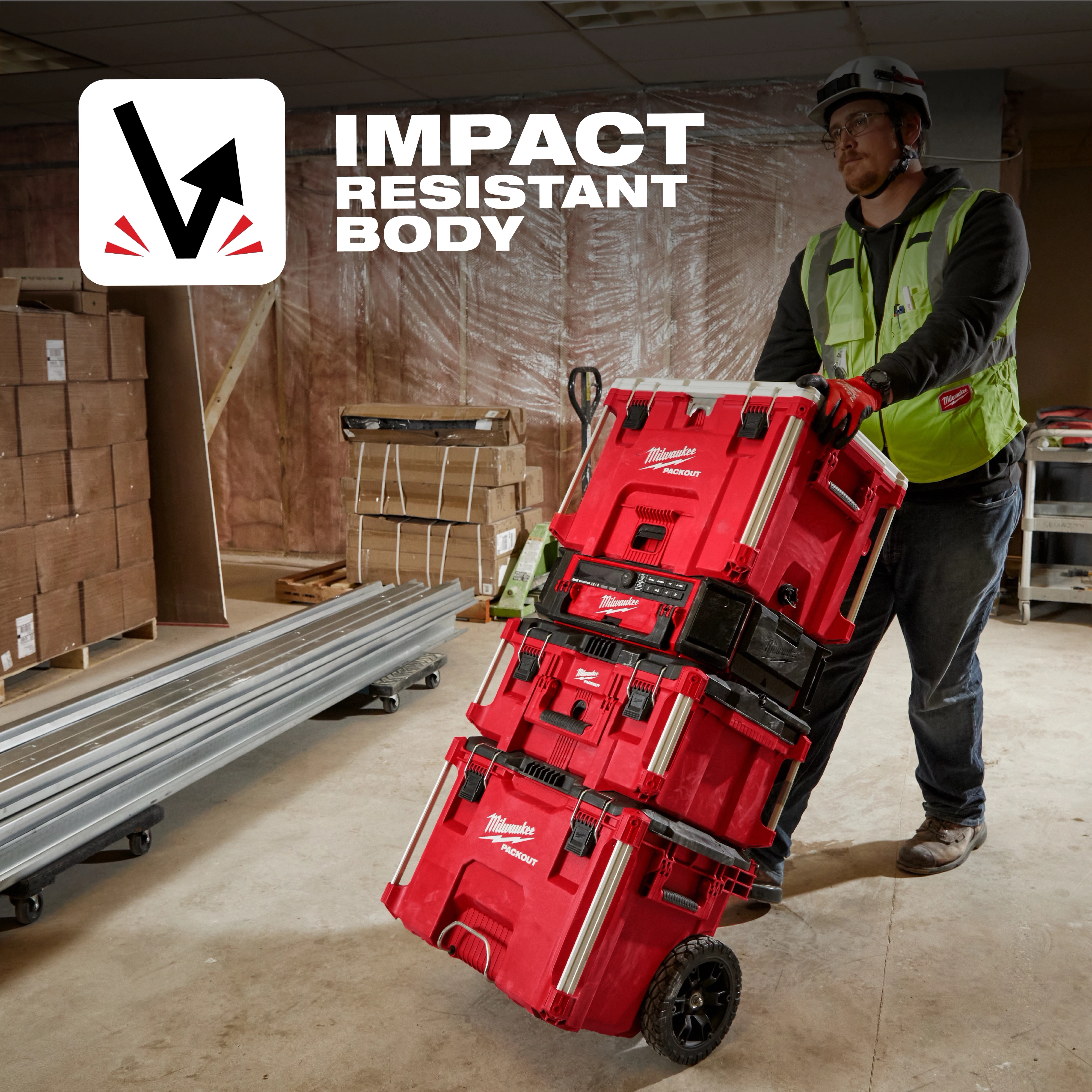 Person in a workshop pulling stacked red PACKOUT 40QT XL Cooler and toolboxes on a cart. Text reads "Impact Resistant Body".
