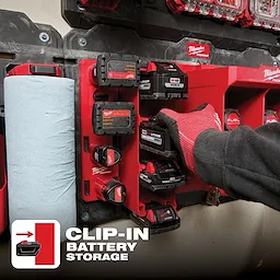 Red Packout M18 Battery Rack shown mounted on a wall holding multiple M18 batteries. Gloved hand accessing a battery. Includes paper towel holder.