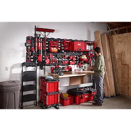 Man organizing tools on a wall-mounted March 2023 Packout Shop Storage system in a well-equipped garage workspace.