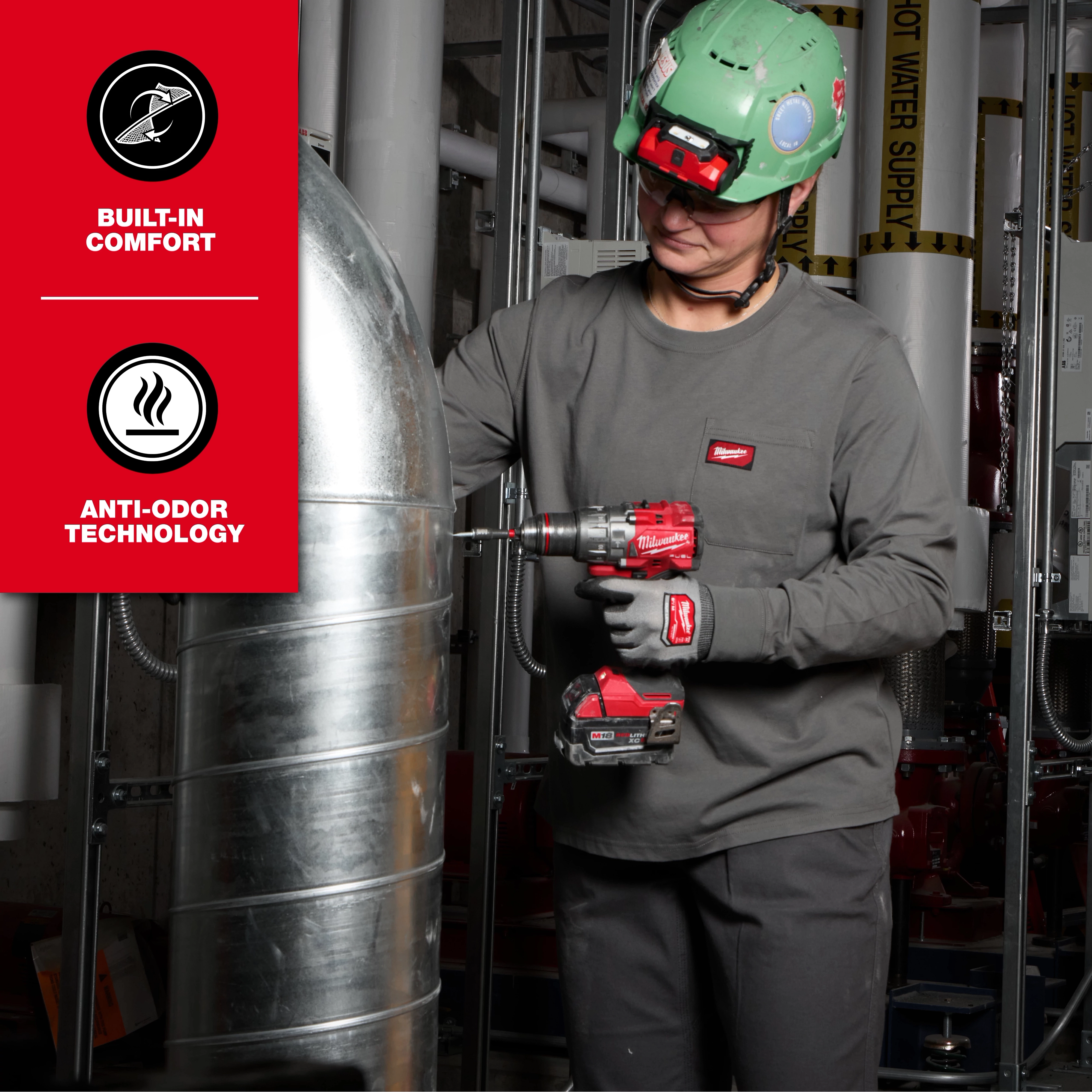 A person uses a red cordless power tool near metal pipes wearing the Women’s GRIDIRON™ Pocket T-Shirt - Long Sleeve. The shirt is dark grey with a pocket. The image highlights built-in comfort and anti-odor technology features of the shirt.